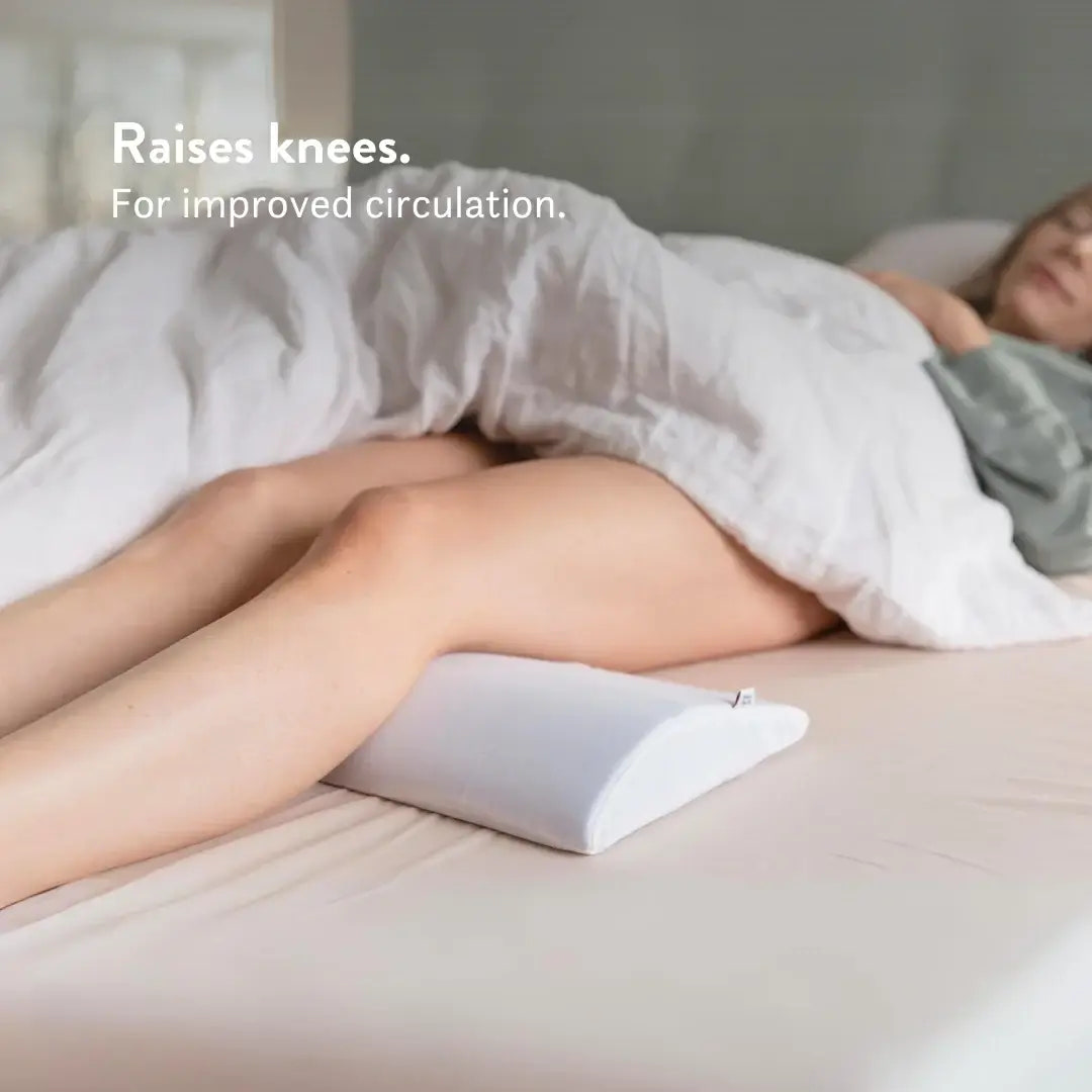 Person lying on a bed with a knee pillow to raise their knees, promoting improved circulation.