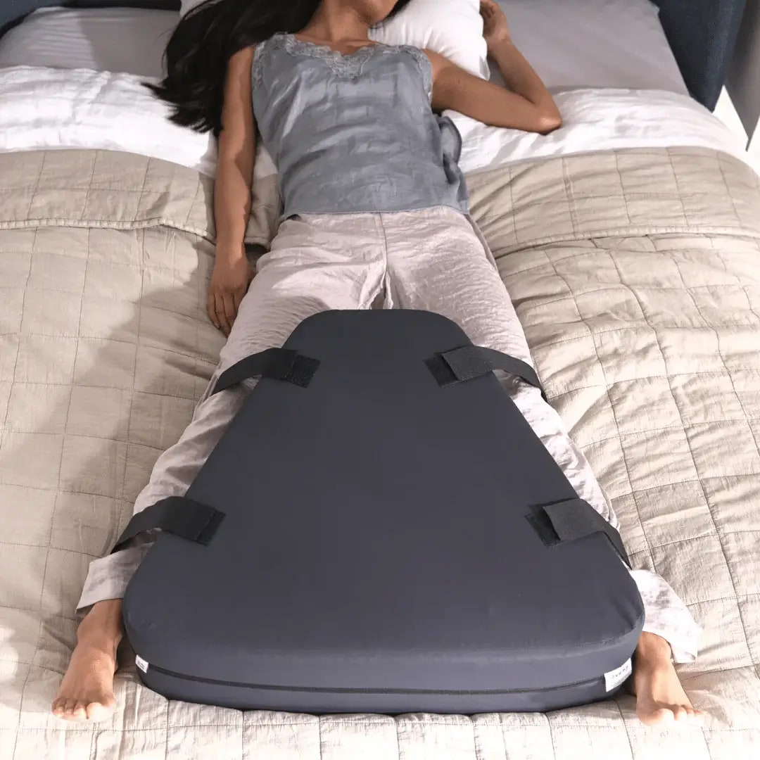 Person lying on a bed with a wedge-shaped pillow under their legs