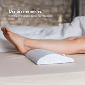 Person using a white elevation pillow to raise ankles on a bed.