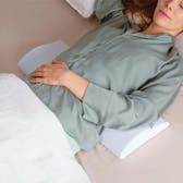 Woman lying on a bed with a green shirt, holding her stomach.