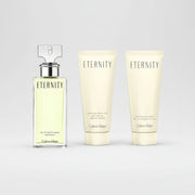 Calvin Klein Eternity gift set containing a 100ml eau de parfum spray bottle, a shower gel tube, and a body lotion tube, all in off-white packaging with black lettering, presented inside a gold-colored box.