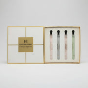 A luxury gift set of four Carolina Herrera Confidential perfume sample vials presented in an open gold-trimmed box next to its white and gold lid.