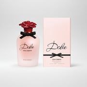 Dolce Roma Rosa Excelsa Eau de Parfum bottle with a pink body, red rose cap, and black ribbon, shown next to its light pink packaging box.