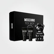Moschino Toy Boy fragrance gift set featuring a large black box, two black body care tubes, and a glossy black bear-shaped bottle with white text, all on a white background.