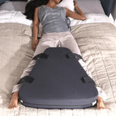 Person lying on a bed with a wedge-shaped pillow under their legs