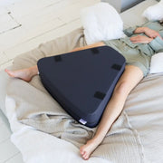 Person lying on a bed with a navy blue wedge-shaped pillow under their legs.