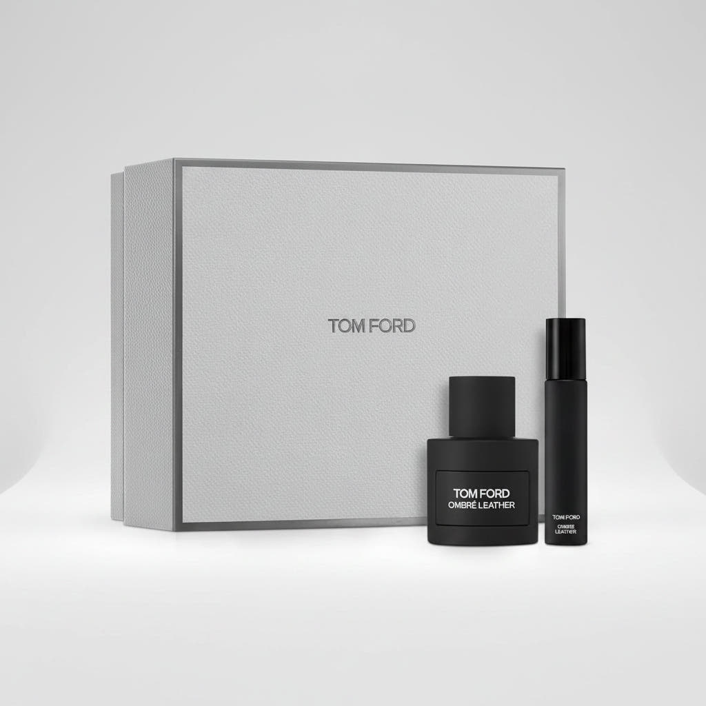 Tom Ford Ombre Leather fragrance set featuring a large textured light gray gift box, a black perfume bottle, and a slim black travel atomizer spray bottle, with a '2 pack' badge in the top right corner.