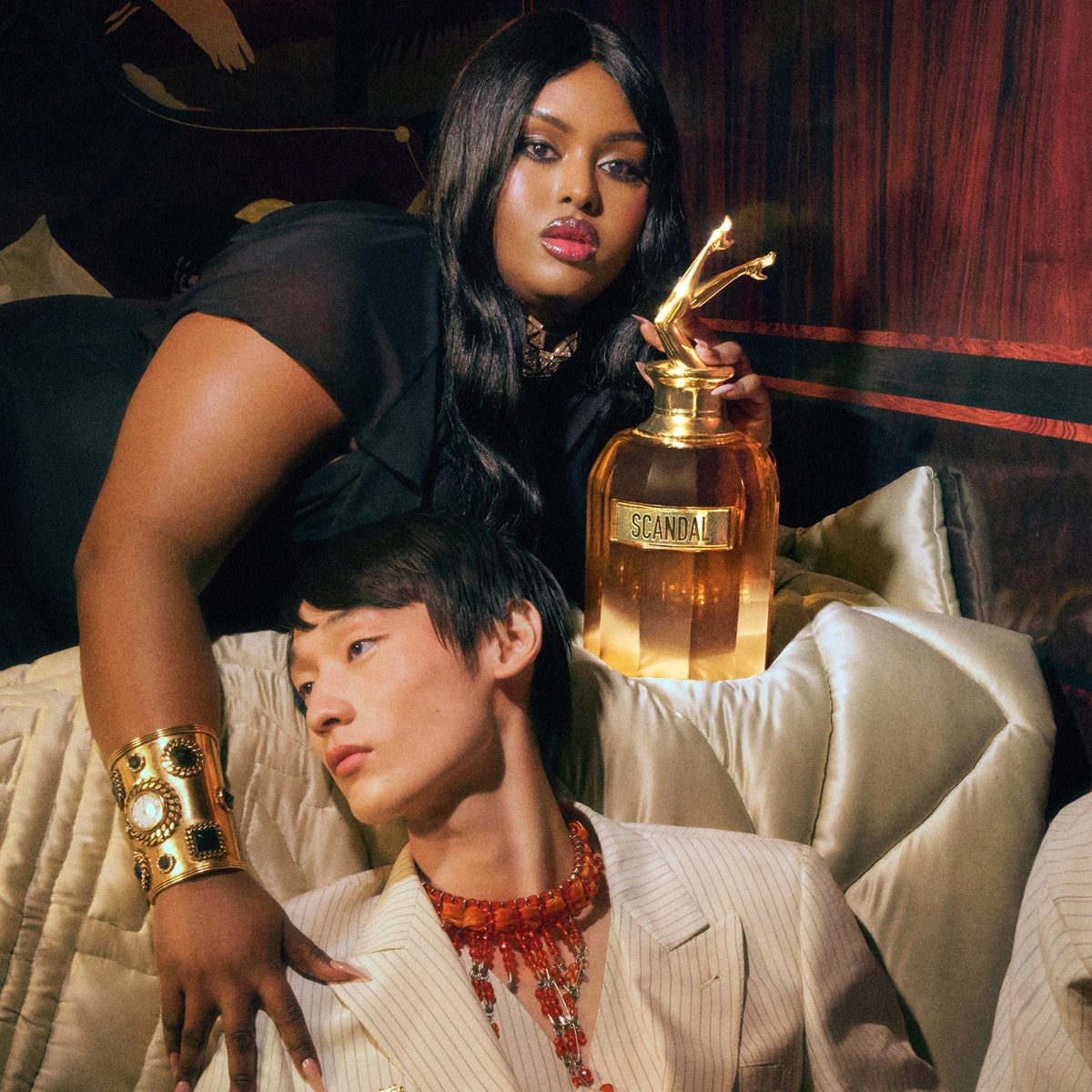 Two  people in a stylish setting with a Jean Paul Gaultier Men's Scandal Absolu Parfum perfume bottle.