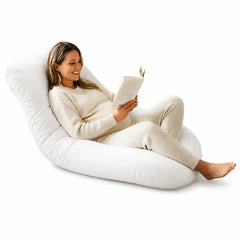 Woman reading a book on a large white pregnancy pillow against a white background
